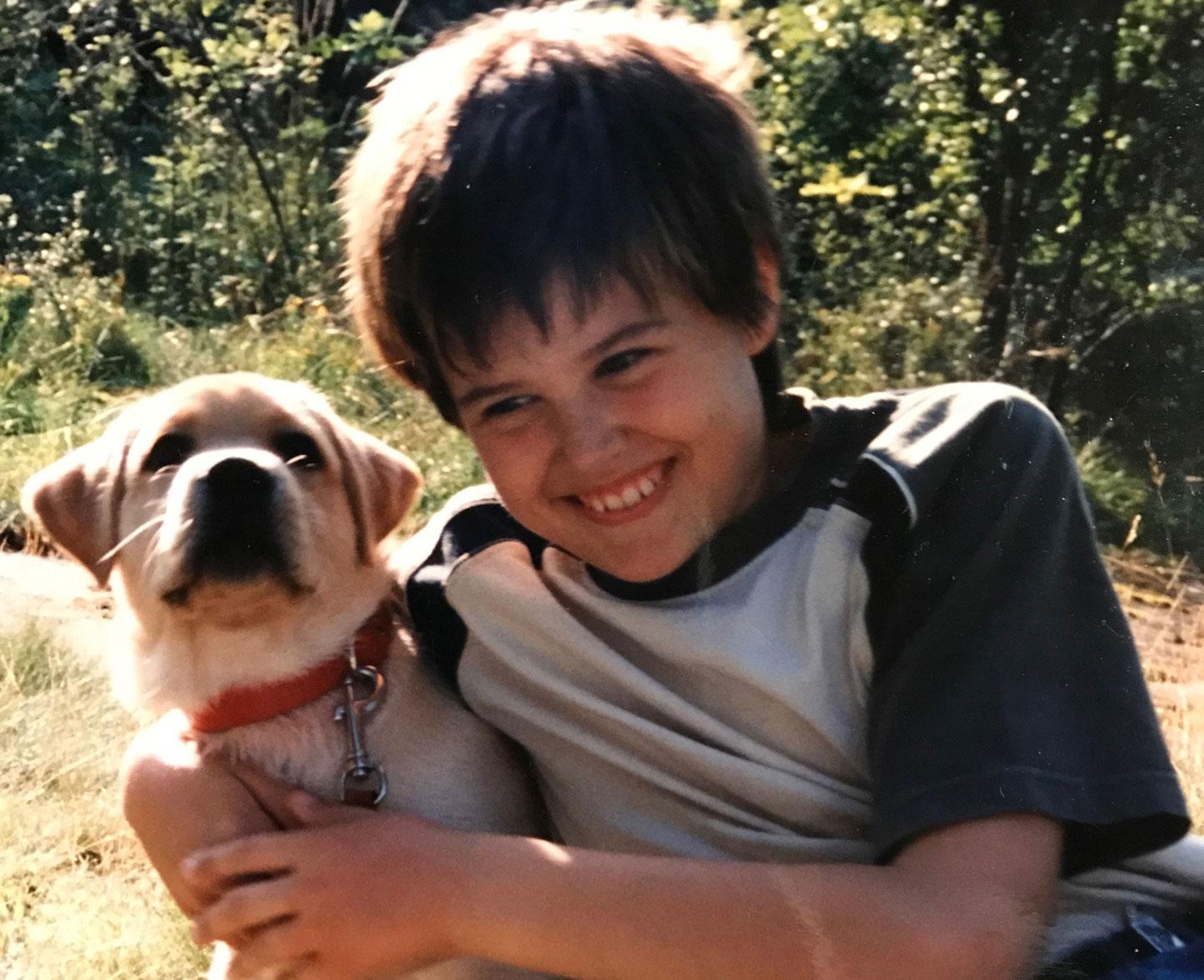 Smiling boy hugging a dog outdoors.